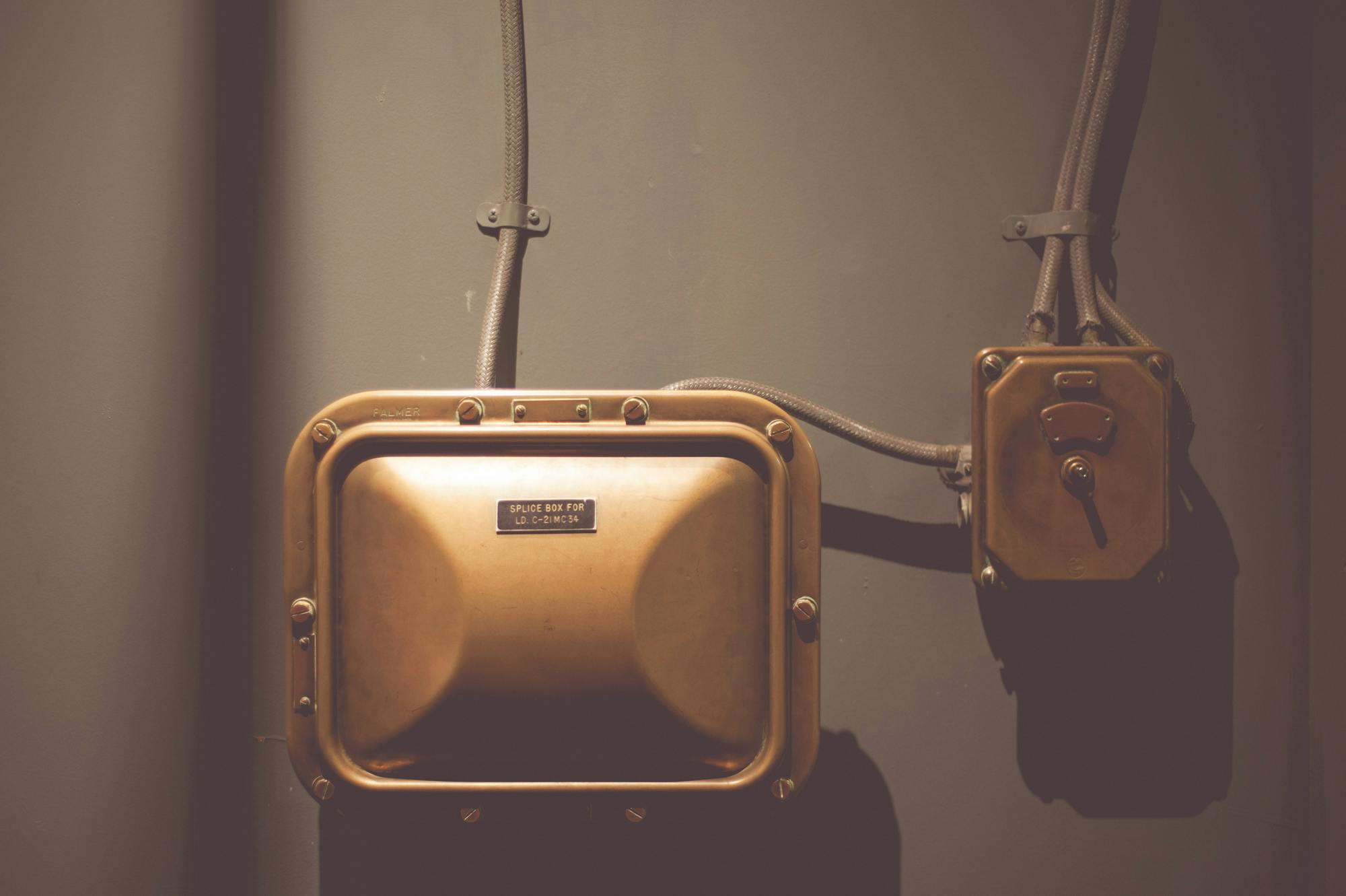Industrial electrical control box with vintage design and copper finish on a wall.