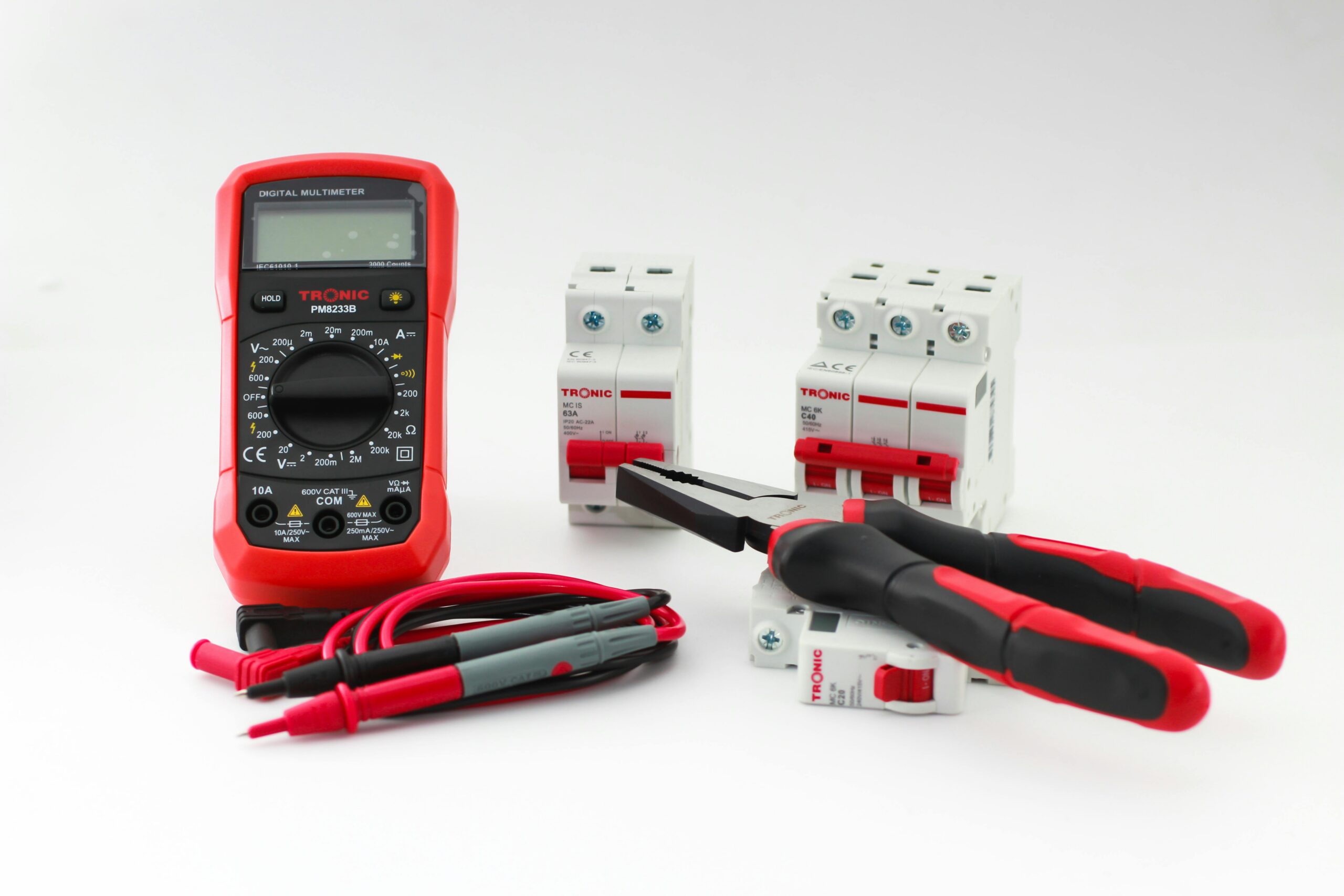 Close-up of a digital multimeter with electrical tools and circuit breakers on a white background.